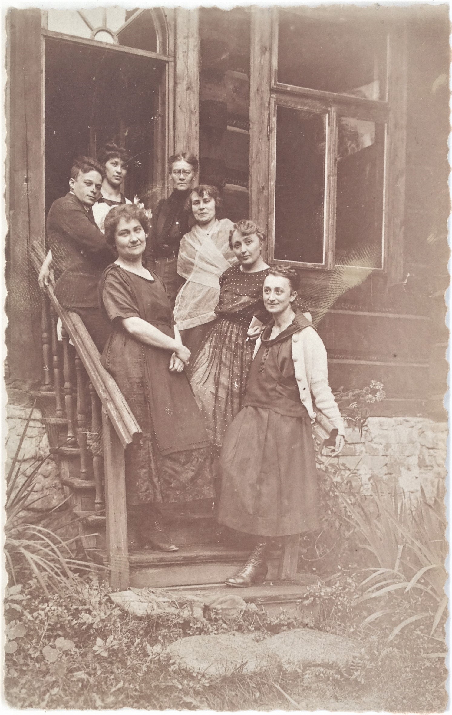 Fotografia czarno-biała. Przedstawia grupę ludzi stojących na schodach domu